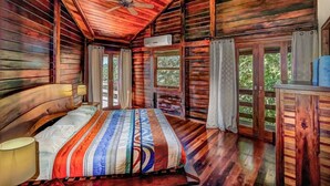 A wooden cabin bedroom with a bed, a ceiling fan, and large windows. - Oceanfront treehouse home w/ private pool, deck, near beach (Tola)