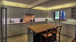 Una cocina con armarios grises, una isla de madera con sillas, una cafetera y un hervidor.