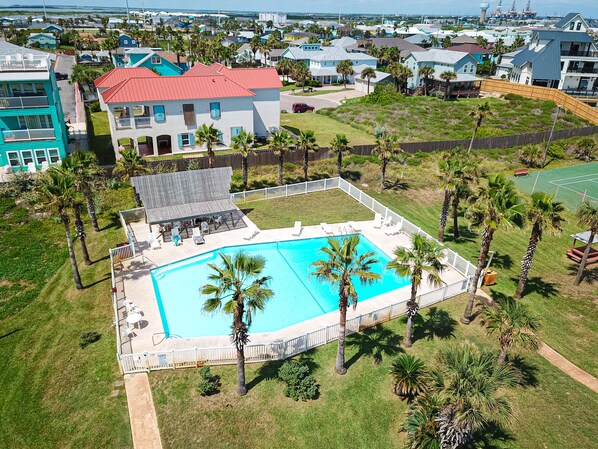 An aerial view of a residential area with a swimming pool surrounded by palm trees and a fenced deck area.