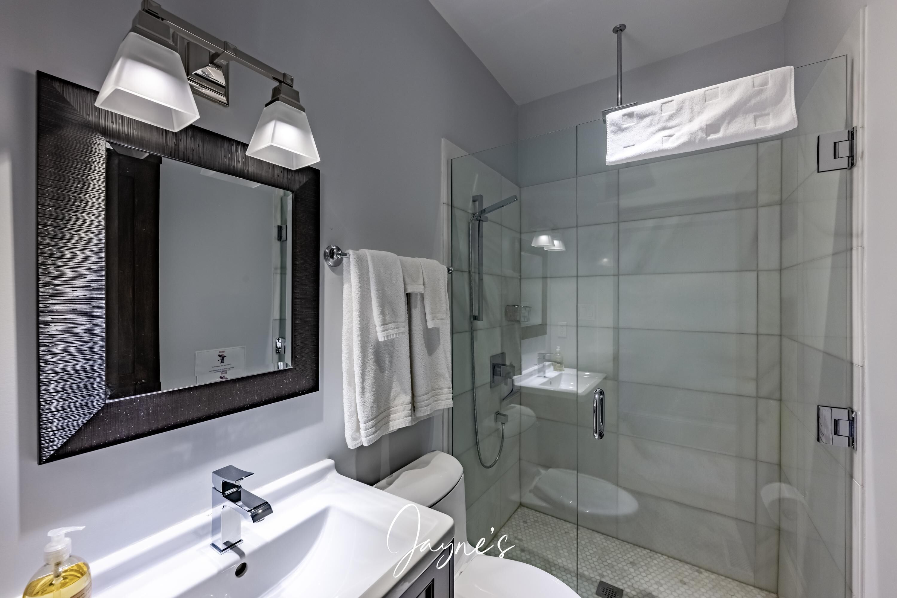 Un baño moderno con cabina de ducha de vidrio, un espejo grande y un lavabo blanco.
