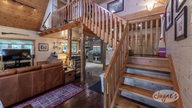 Un interior de madera con una escalera, una sala de estar con un sofá de cuero marrón y una zona de cocina.