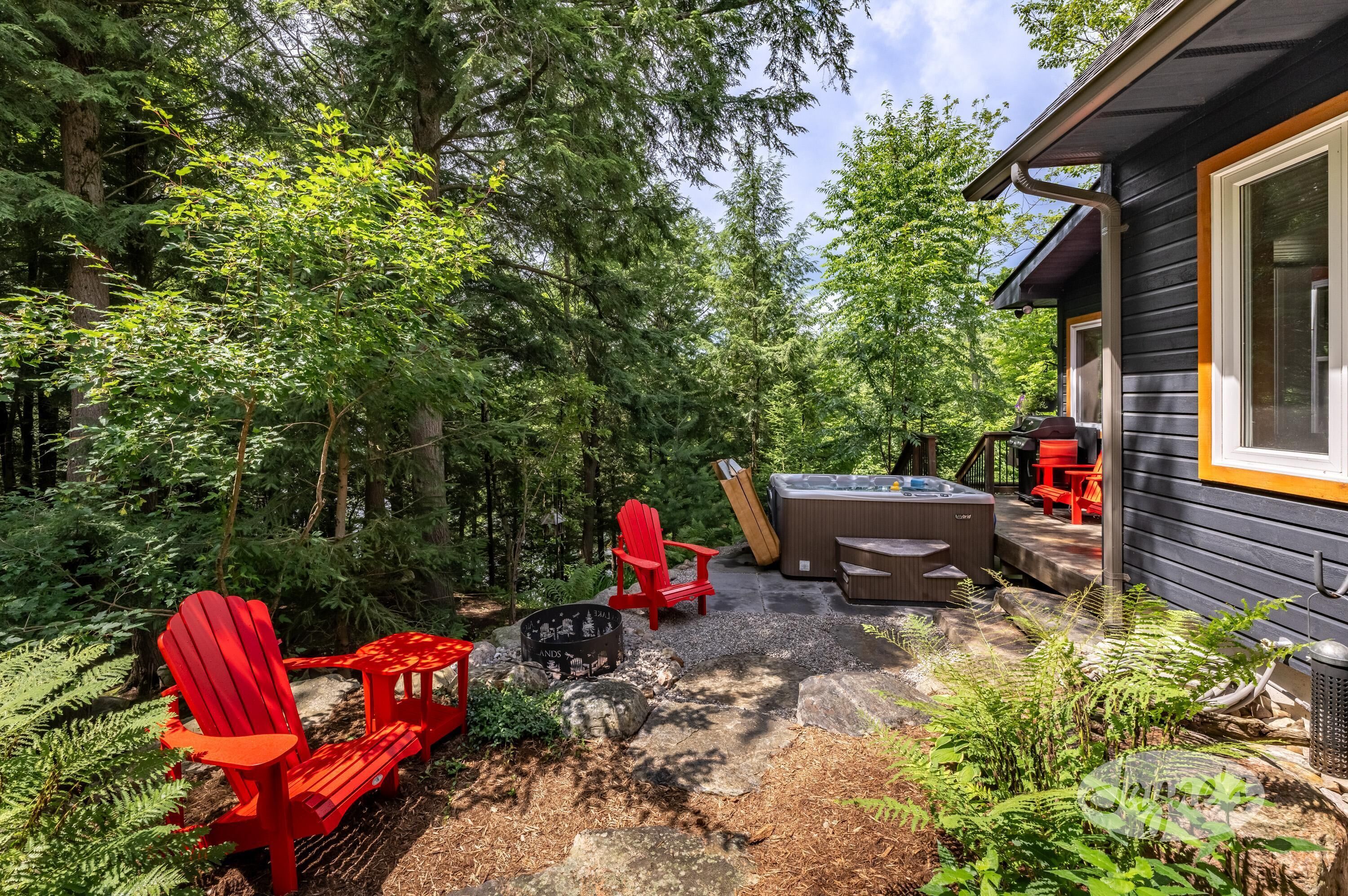 Eine Holzterrasse mit Adirondack-Stühlen, einem Whirlpool und einer Steinkaminfeuerstelle.