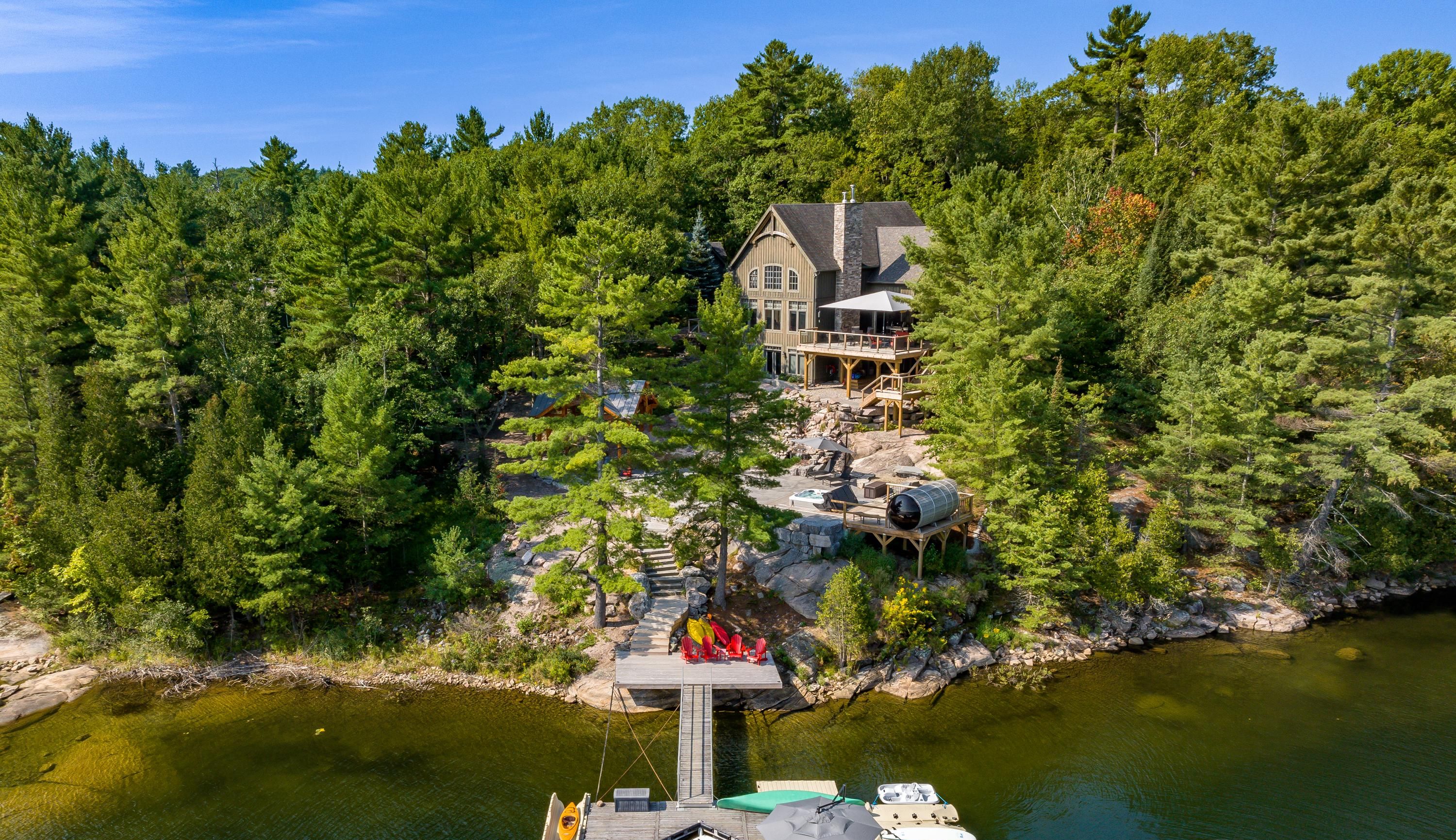 A lakeside property with a dock, boats, and a large house surrounded by dense forest.