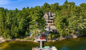 Une propriété au bord du lac, dotée d’un quai, de bateaux et d’une grande maison entourée d’une forêt dense.