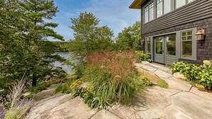 A modern house with a stone pathway leading to a dock by a lake. - Gorgeous 6 bedroom | 6 bathroom cottage with living quarters in Boathouse! (Seguin)