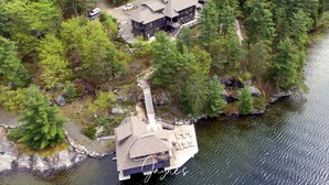 An aerial view of a lakeside property with a large house and a dock extending into the water. - Gorgeous 6 bedroom | 6 bathroom cottage with living quarters in Boathouse! (Seguin)