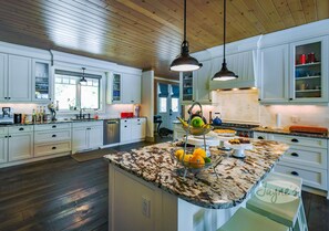 Une cuisine spacieuse avec des meubles blancs, un plan de travail en granit et des luminaires suspendus.