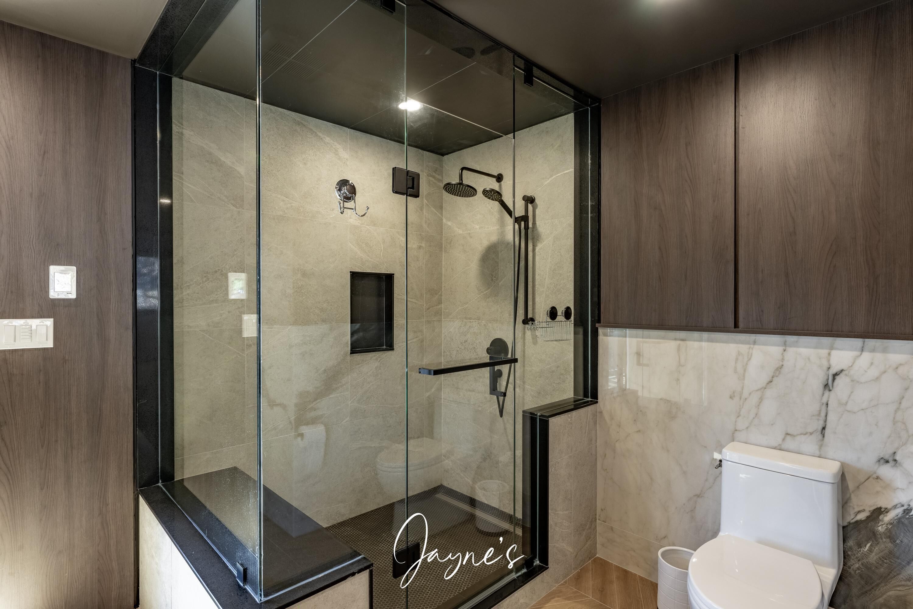 Un baño moderno con ducha envuelta en cristal, inodoro blanco y paneles de madera.
