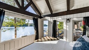 Ein Zimmer mit großem Fenster und Seeblick, ein Bett mit gemustertem Kissen und Blick ins Freie.