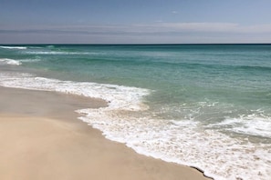 Ein Strand mit klarem türkisblauem Wasser und weißen Schaumwellen.