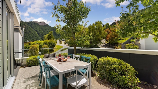 A patio with a table and chairs, surrounded by greenery and a mountain view.
