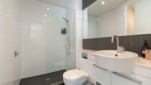 A modern bathroom with a glass-enclosed shower, a white toilet, and a sink with a mirror above it.