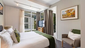A hotel room with a bed, a chair, a TV, and a painting.