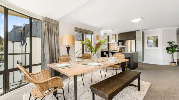 A dining area with a wooden table set for four, surrounded by wicker chairs, a bench, and a vase with flowers. - Central Luxury at 408 The Beacon | Hot Tub | 2 Bed | 2 Bath (Queenstown)