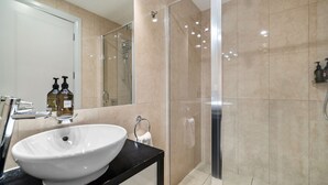 A modern bathroom with a large white sink, a glass shower enclosure, and beige tiled walls. - Lakefront at 911 The Beacon | Studio (Queenstown)