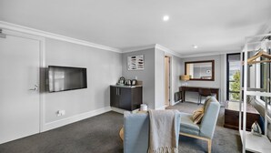 A modern hotel room with a flat-screen TV, a dark wooden wardrobe, a desk with a chair, and a large window offering a view of the outdoors. - Lakefront at 911 The Beacon | Studio (Queenstown)