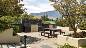 An outdoor patio with a stone barbecue, two wooden tables, and a stone wall.