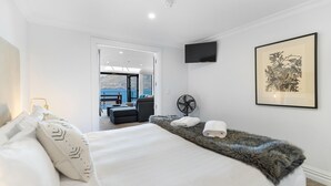 Un dormitorio con una cama grande, vistas a un área de estar exterior, un televisor montado y una obra de arte enmarcada en la pared.
