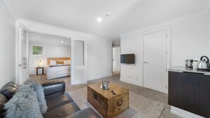 Een hotelkamer met een bed, een televisie, een kitchenette, een houten kist en een leren bank.
