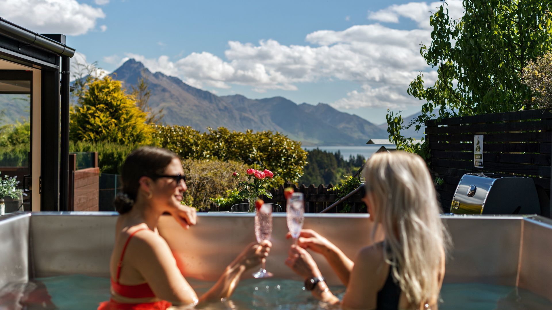 Two people toasting with champagne glasses in a hot tub with a mountain view.