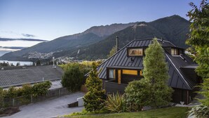 Una casa moderna con techo inclinado, un tragaluz visible en el ático y vista a un lago y montañas al fondo.