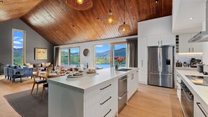 A modern kitchen with a large island, stainless steel appliances, and a view of a lake and mountains. - Sicilian Luxury Retreat 2 | Alfresco Dining | Close to Wineries (Queenstown)