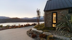 A stone house with a dark roof, a stone pathway, and a view of a lake and mountains. - Sicilian Luxury Retreat 2 | Alfresco Dining | Close to Wineries (Queenstown)
