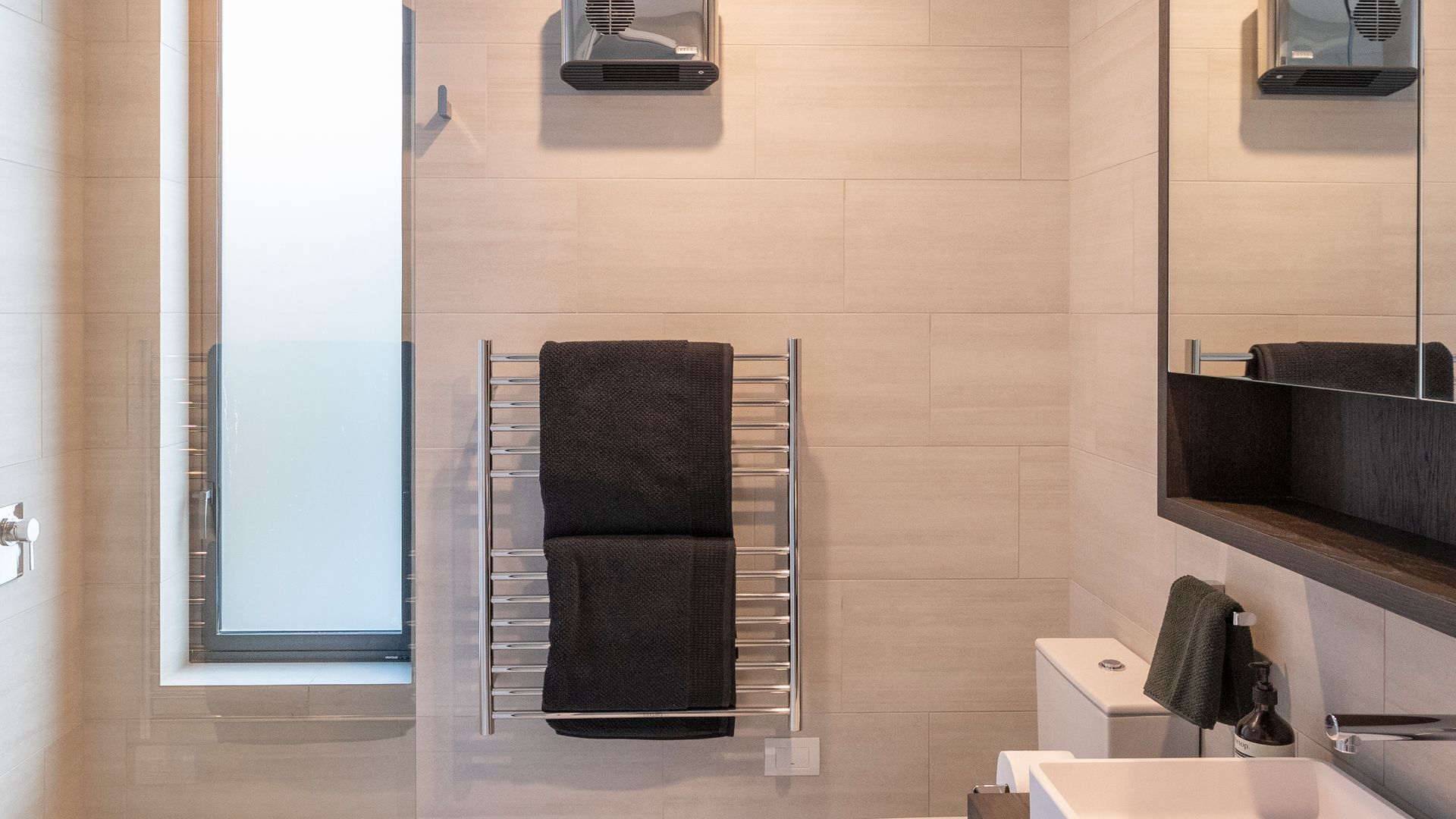 Een moderne badkamer met een handdoekhouder, een toilet, een wastafel en een spiegel.