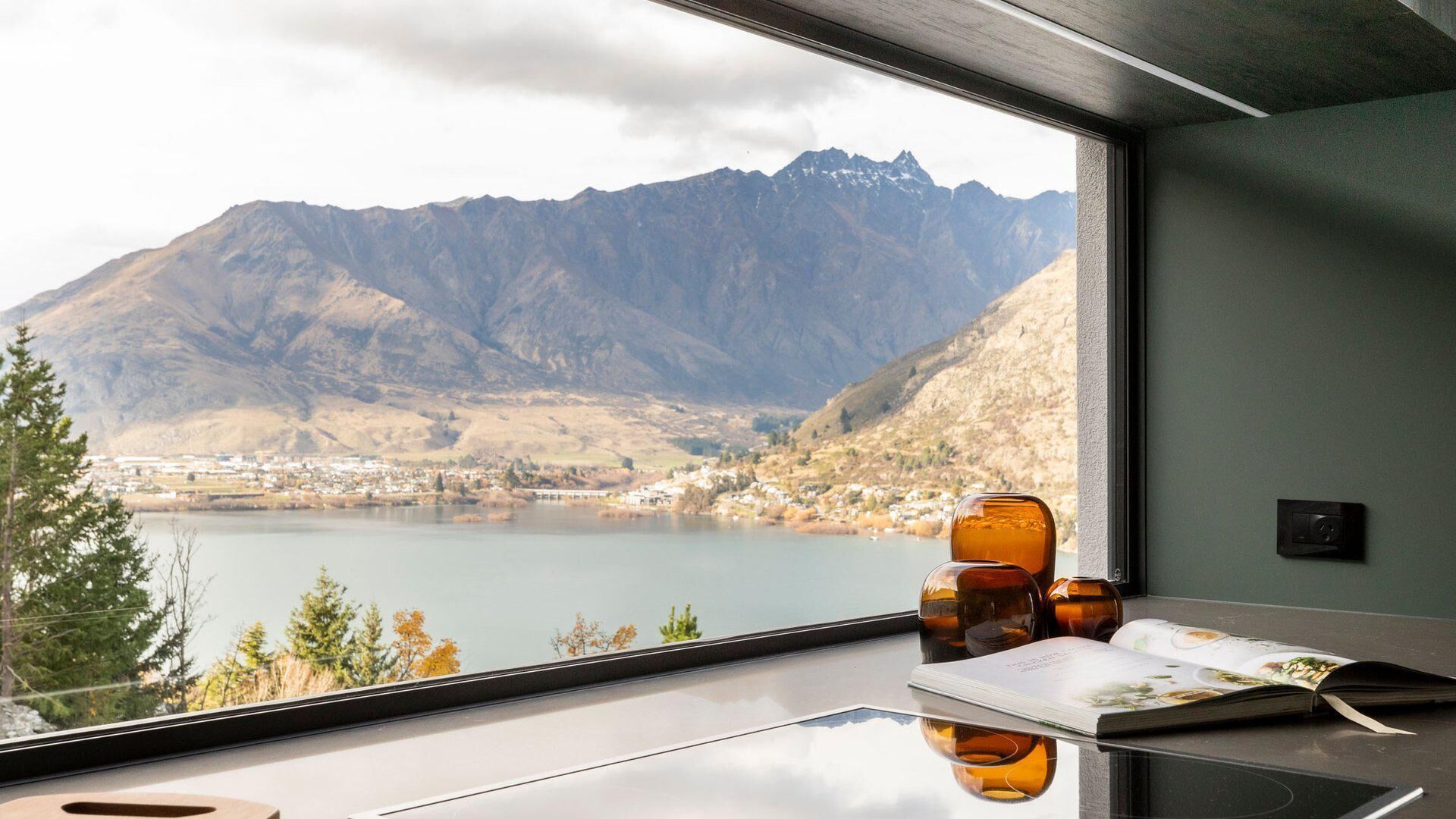 Een kamer met een groot raam met uitzicht op een meer en bergen.