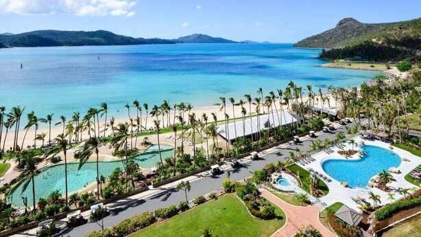 Un resort con una gran piscina, una playa con palmeras y vistas al océano.