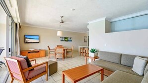 Amplia sala de estar con sofá, mesa de centro y comedor. Hay un televisor montado en la pared y una ventana que ofrece vistas.
