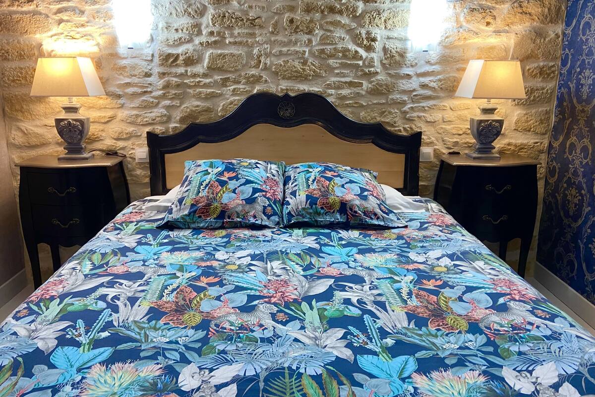 Een kamer met een stenen muur, een bed met bloemenbeddels, twee nachtkastjes met lampen en een kamerkleed met dessin.