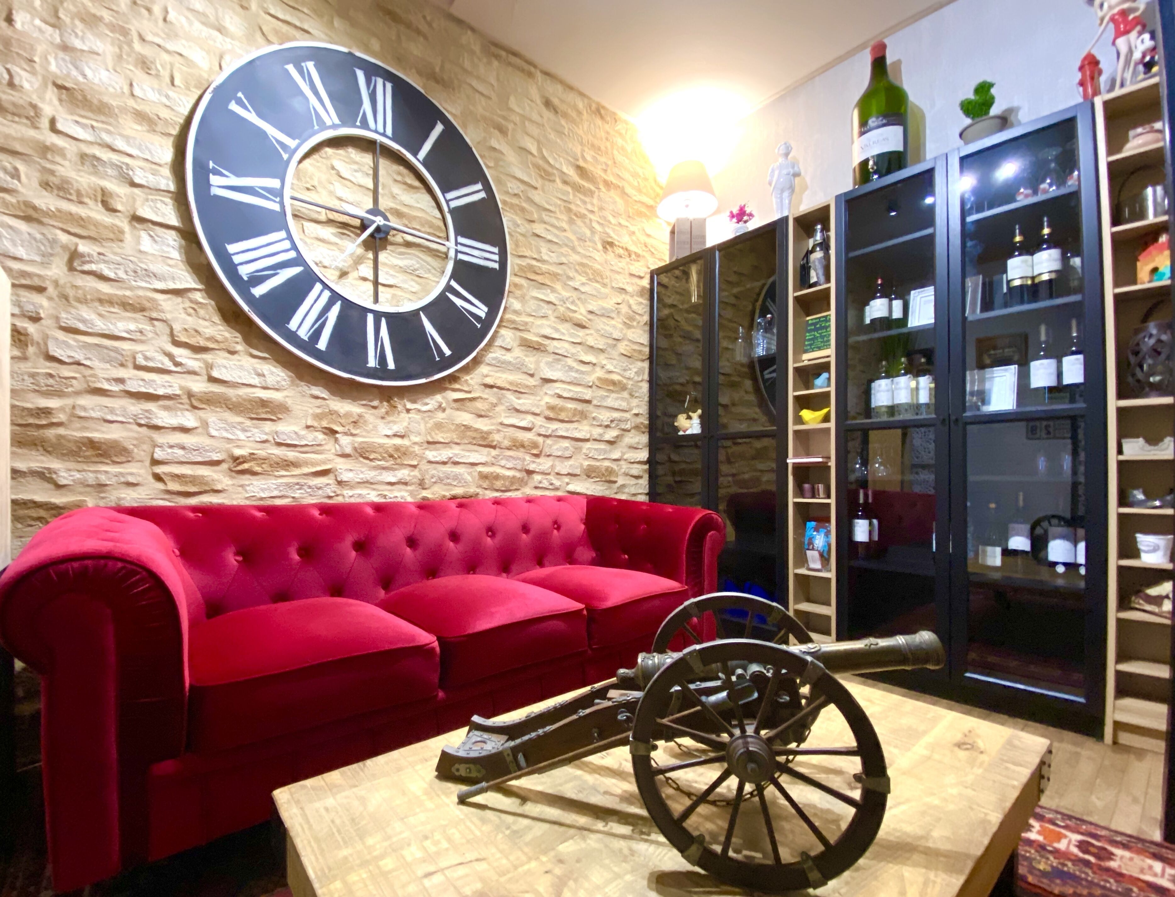 A red sofa, a large wall clock, and a wine cabinet with bottles.