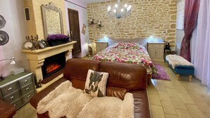A cozy bedroom with a stone wall, a fireplace, a chandelier, and a bed with floral bedding. - Ô Clair de Lune - Espace bien être avec Spa - Piscine chauffée (Sarlat-la-Canéda)