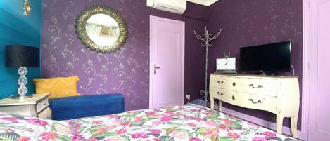 Un dormitorio con colcha estampada, televisor en una cómoda, espejo en la pared y una puerta.