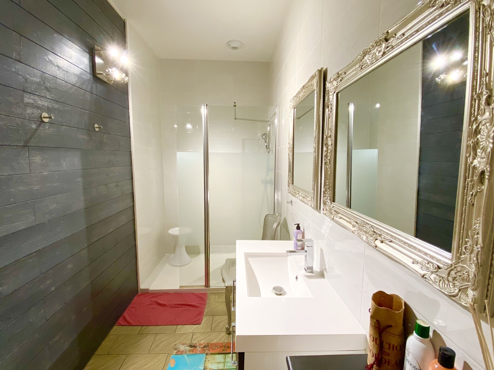 Une salle de bain moderne avec une douche à l’italienne en verre, un lavabo blanc et un grand miroir décoratif.