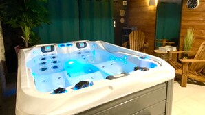 A hot tub with multiple jets, surrounded by wooden walls and a small table with chairs. - Ô Clair de Lune - Espace bien être avec Spa - Piscine chauffée (Sarlat-la-Canéda)