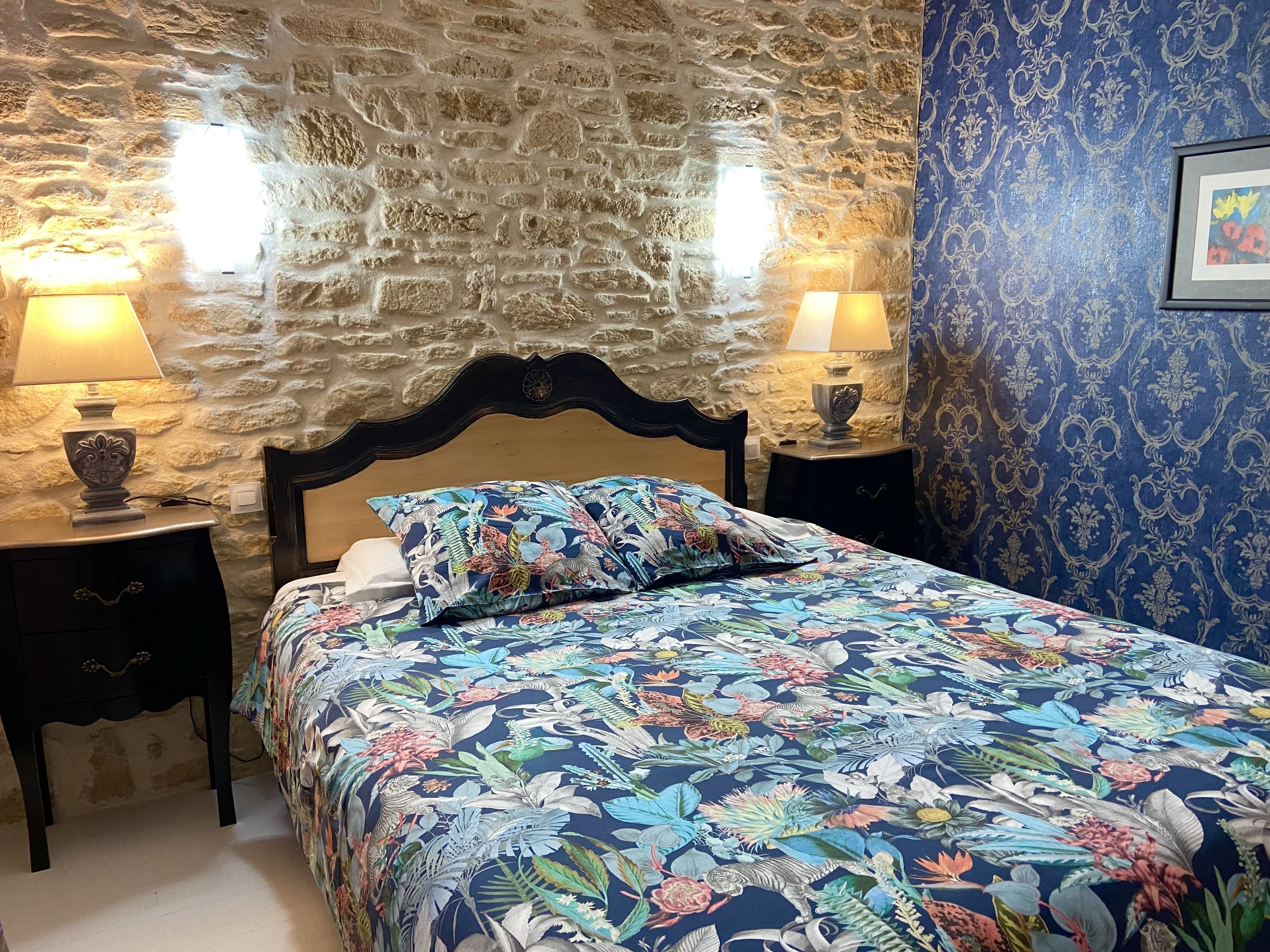 A bedroom with a stone wall, floral bedspread, two bedside lamps, and a patterned wall.