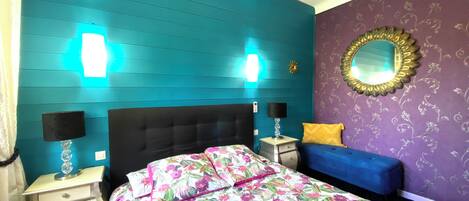 A bedroom with teal walls, a floral bedspread, a blue sofa, and a decorative mirror.
