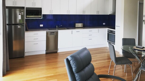 A modern kitchen with white cabinets, a blue backsplash, and stainless steel appliances.