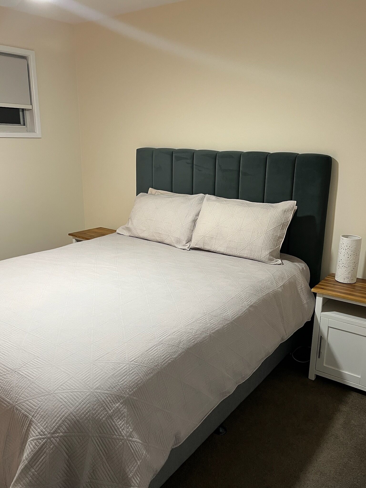 Un lit simple avec une tête de lit sombre, du linge de lit blanc et une table de chevet avec une lampe.