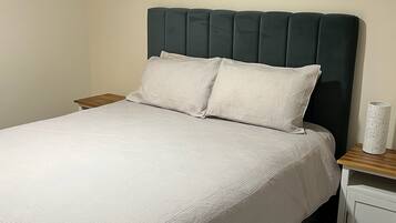 Un lit simple avec une tête de lit sombre, du linge de lit blanc et une table de chevet avec une lampe.
