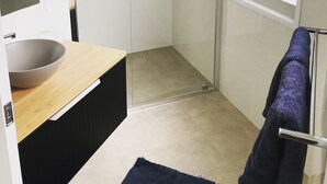 A modern bathroom with a glass shower enclosure, a sink with a bowl, and a towel rack with a towel.
