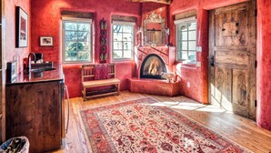 A cozy room with a fireplace, wooden beams, and a red wall. - Casa Poco Joya | Cozy Santa Fe Gem with Views (Santa Fe)