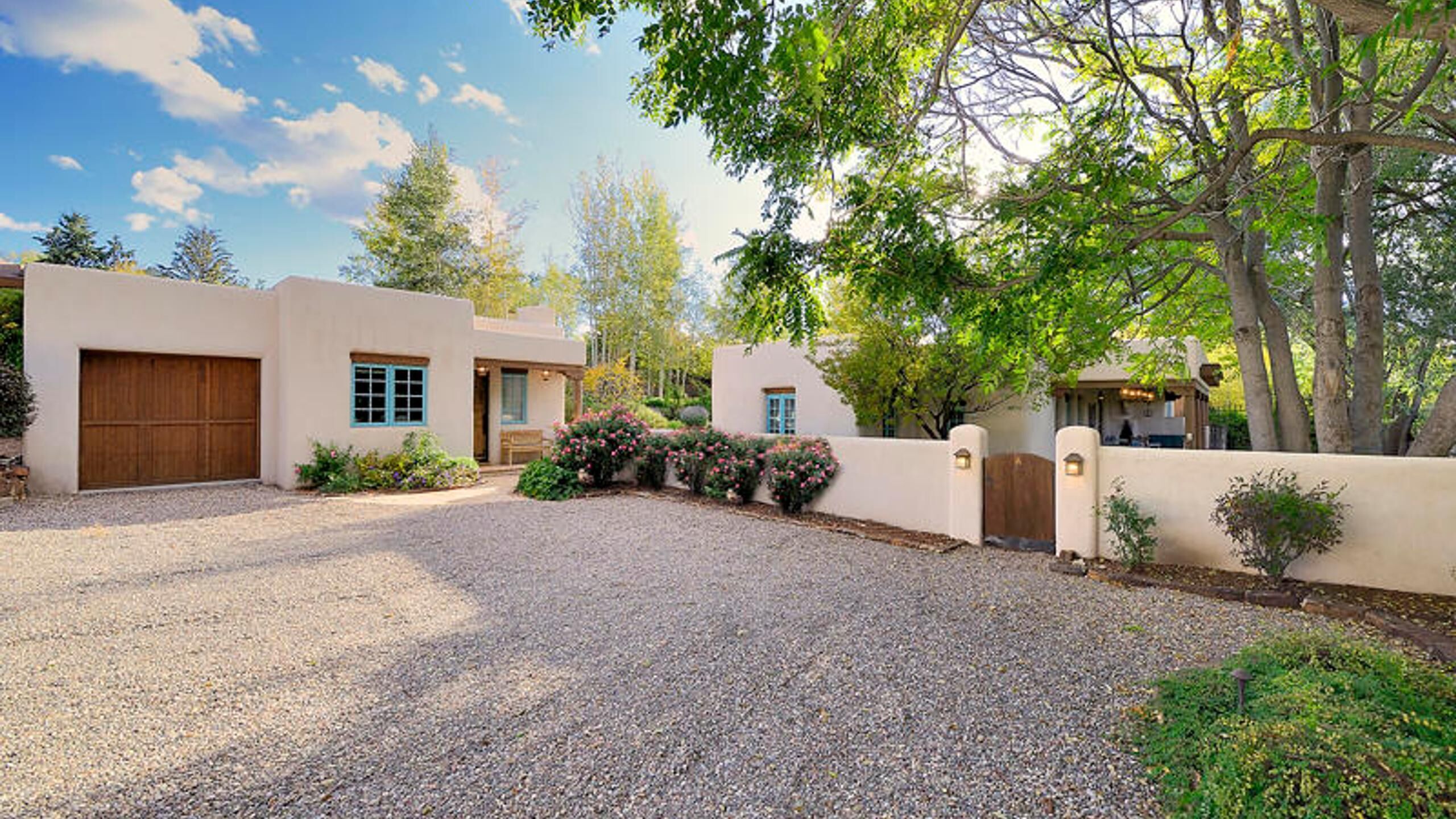A residential property with a gravel driveway, a wooden garage door, and a landscaped garden with shrubs and flowers.