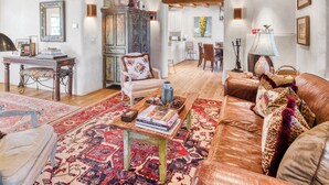A spacious living room with a wooden ceiling, a sofa, a coffee table with books, and a patterned rug. - Casa Poco Joya | Cozy Santa Fe Gem with Views (Santa Fe)