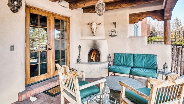 A cozy outdoor seating area with a fireplace, wooden furniture, and a rustic stone wall. - Casa Poco Joya | Cozy Santa Fe Gem with Views (Santa Fe)