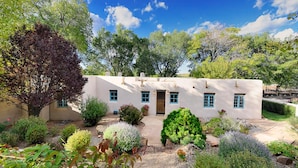A stucco building with a flat roof, a central door, and multiple windows with blue trim. - Casa Poco Joya | Cozy Santa Fe Gem with Views (Santa Fe)
