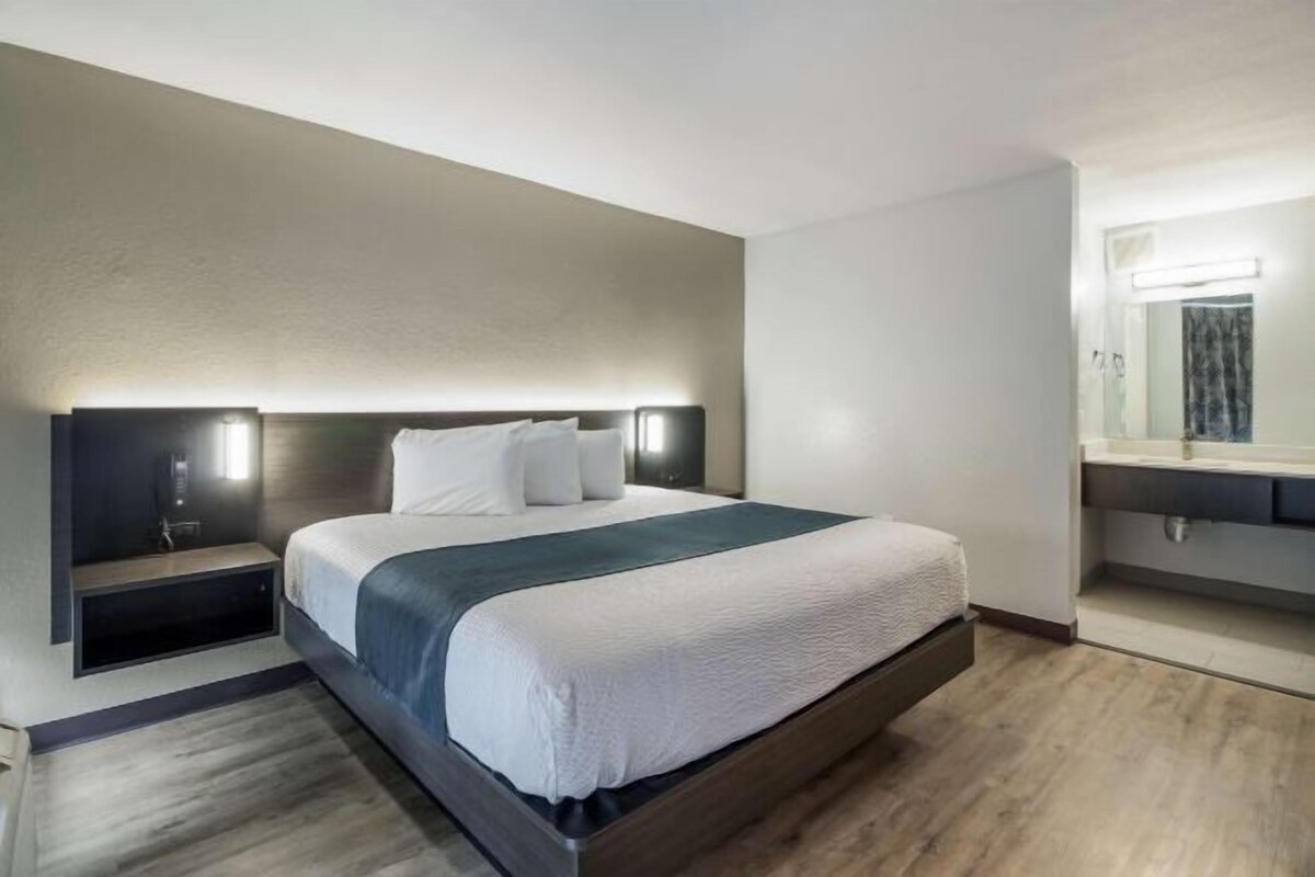 A hotel room with a large bed, bedside tables, a mirror, and a wooden floor.