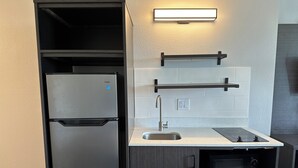 A compact kitchen with a stainless steel refrigerator, a built-in oven, a sink, and a countertop with a range hood. - Motel 6 Groves, TX (Groves)